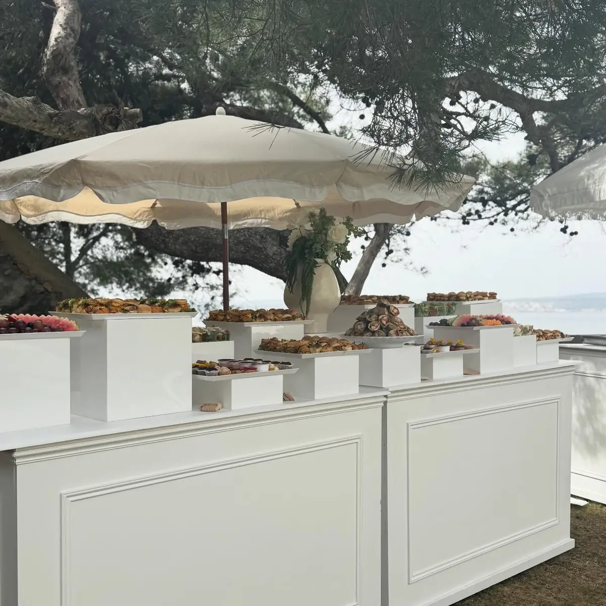 Buffet Sweet Cook installé en bord de mer sous les pins, avec parasols blancs