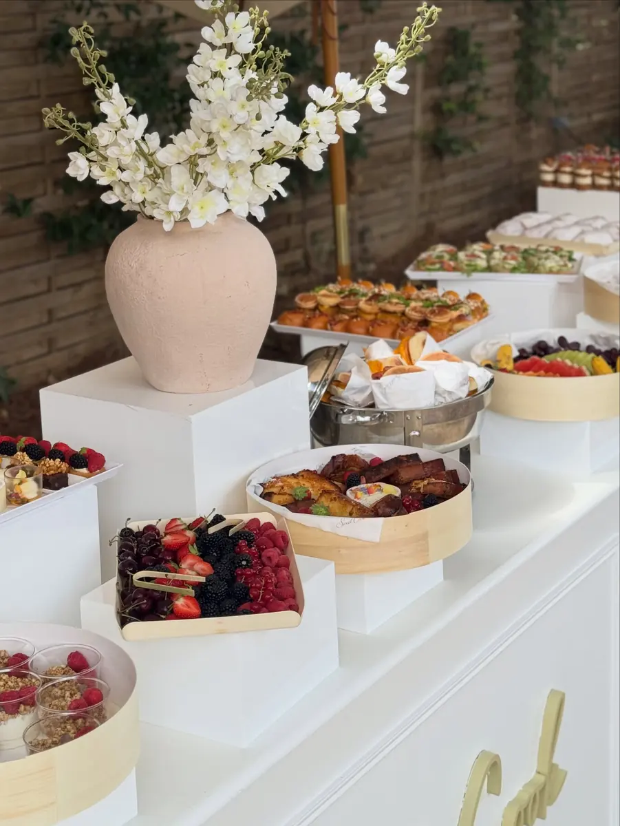 Buffet brunch dans un jardin : fruits rouges, viennoiseries et vase de fleurs blanches
